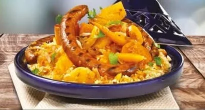 Couscous servi dans un plat à tajine bleu avec merguez et légumes